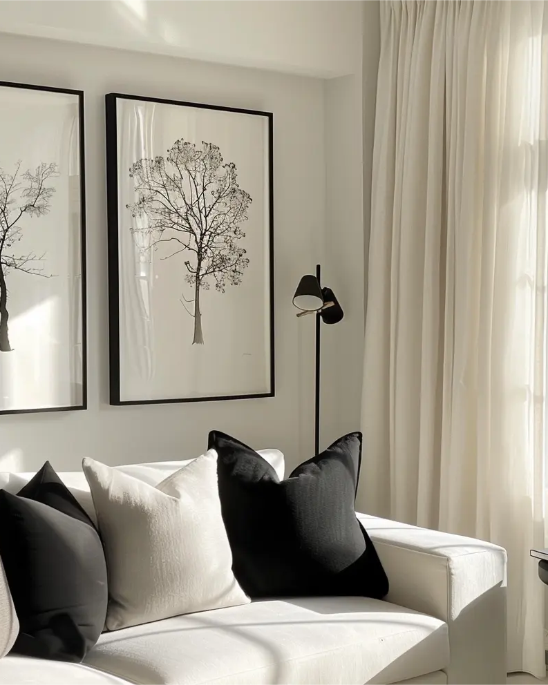 Modern living room with white drapery, black and white pillows, and minimalist tree art on the wall.