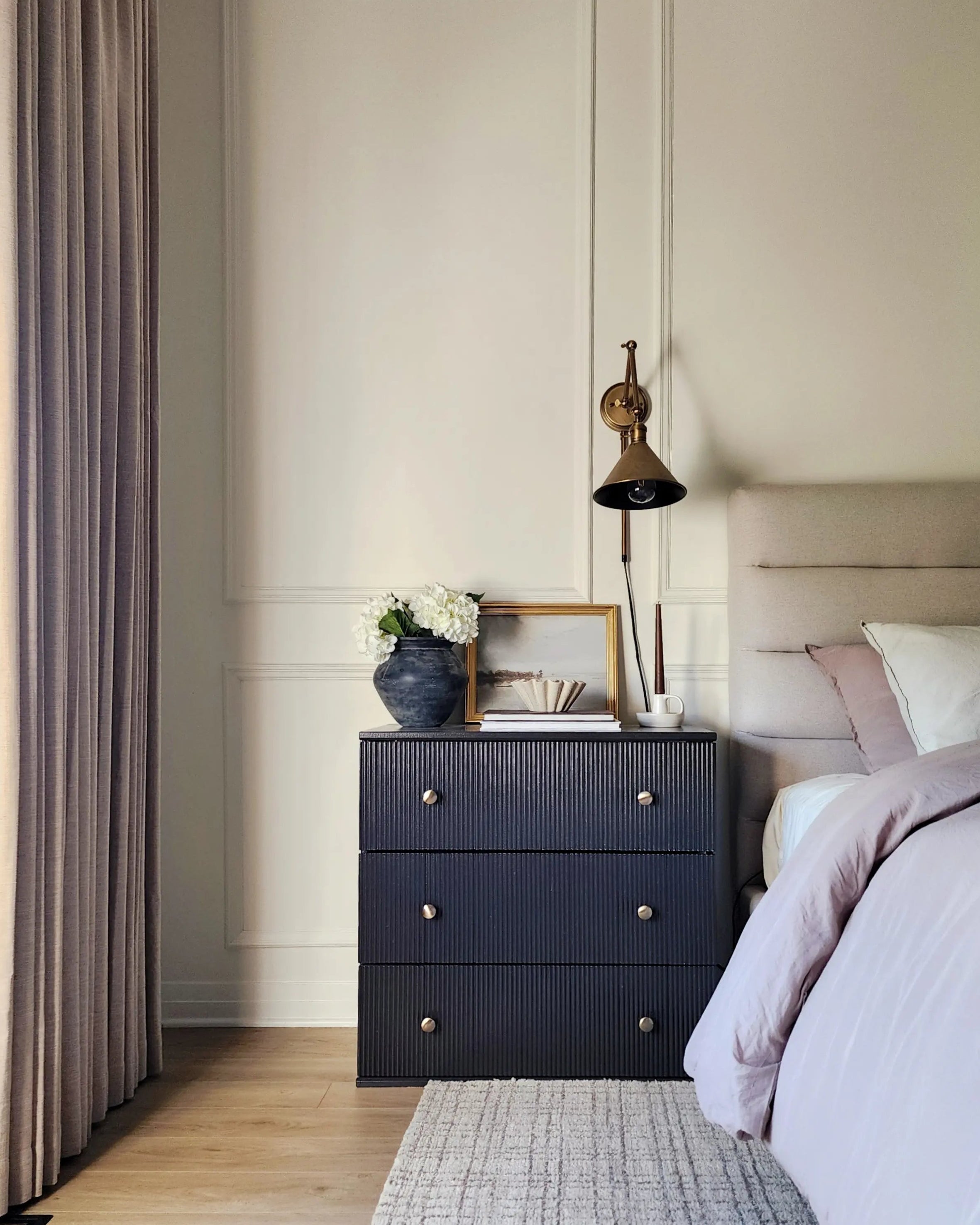 Pleated curtains in a soft neutral tone frame the window, adding texture and elegance to the modern bedroom decor